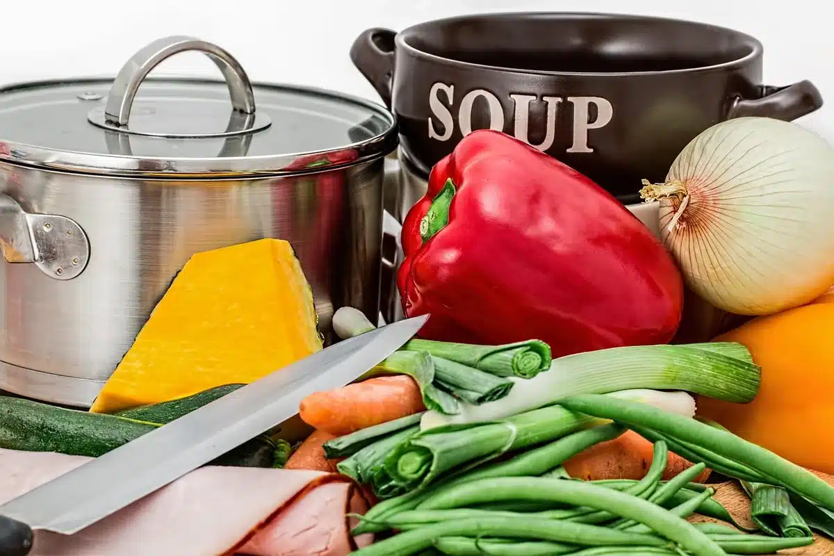 Personne découpe des légumes à côté d'une casserole de soupe qui mijote